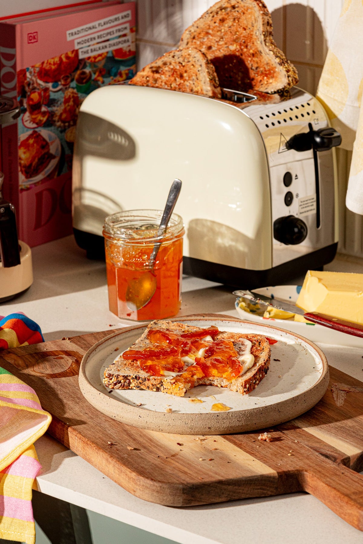 Toasted sandwich on a plate with a jar of jam, toaster, and kitchen items in the background.