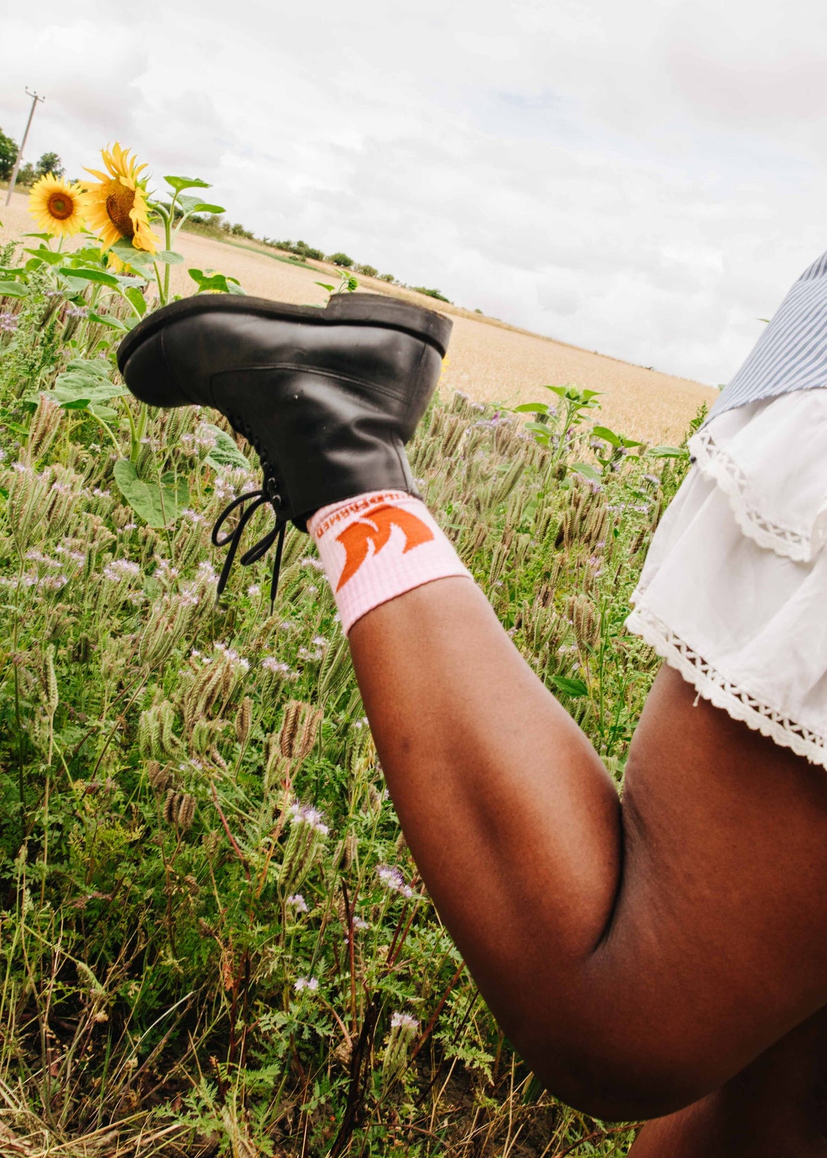Person wearing black boots and a white skirt with Wildfarmed regen socks in a field with sunflowers.